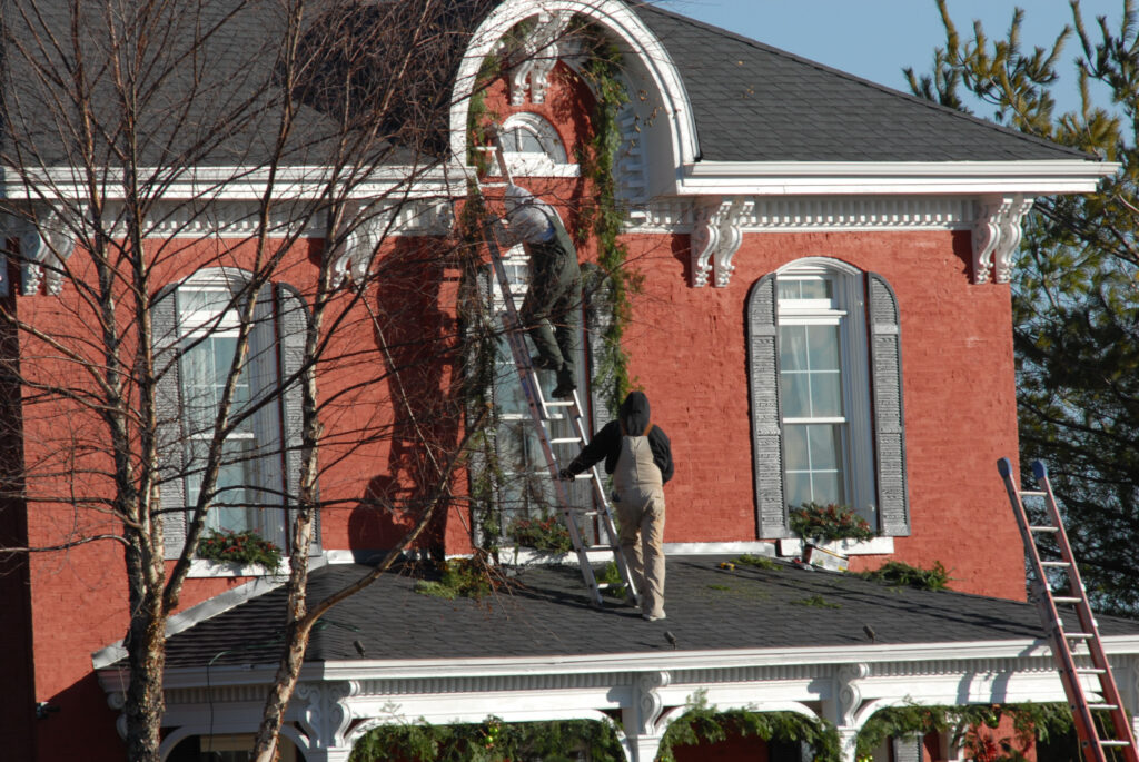 Worker on ladder cleaning gutters on two-story brick home in Nashville